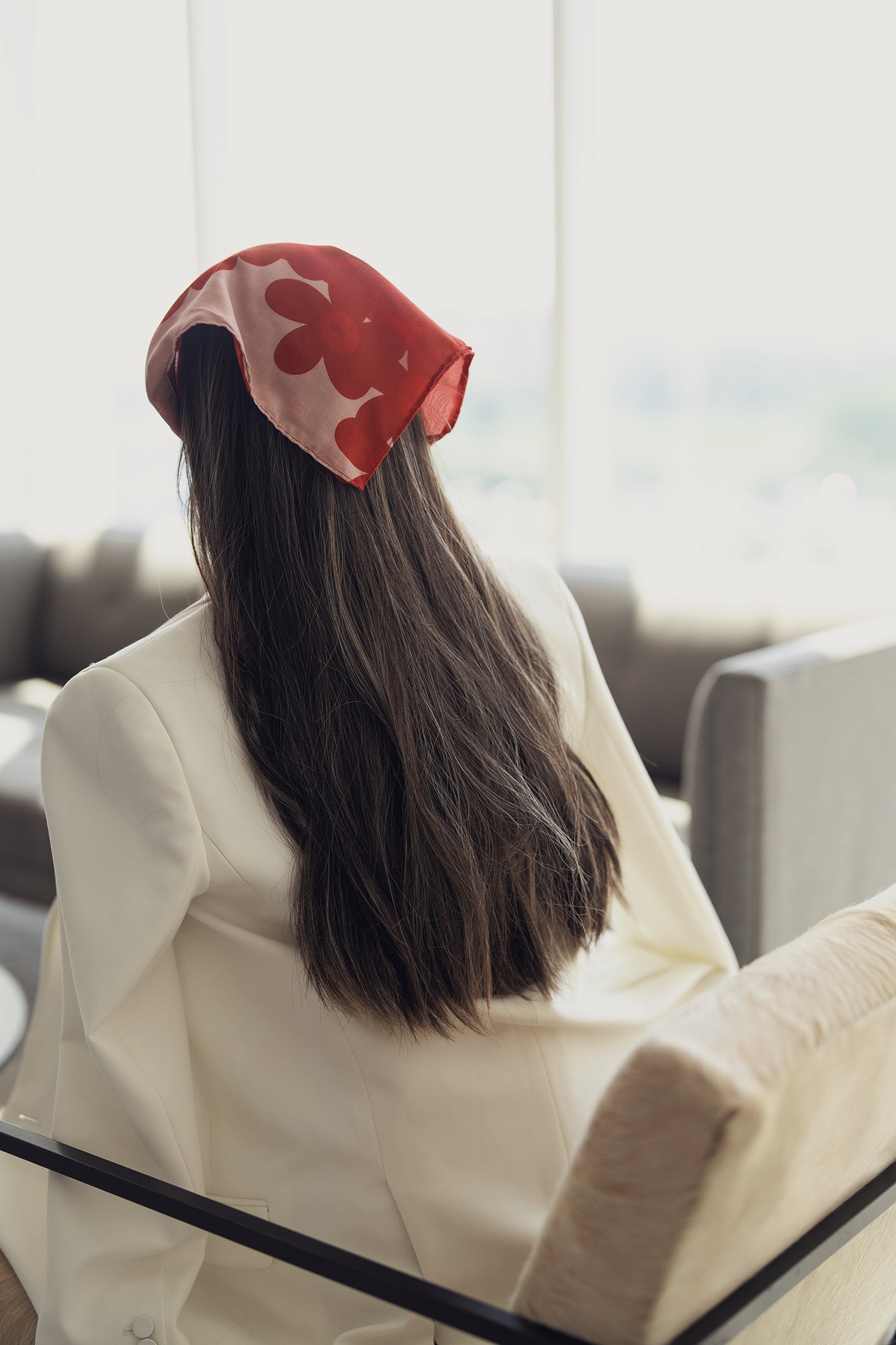 Red and blush pink bandana with bold floral silhouettes, draped over the head and flowing with long dark hair, adding a soft, artistic contrast to a crisp white blazer.