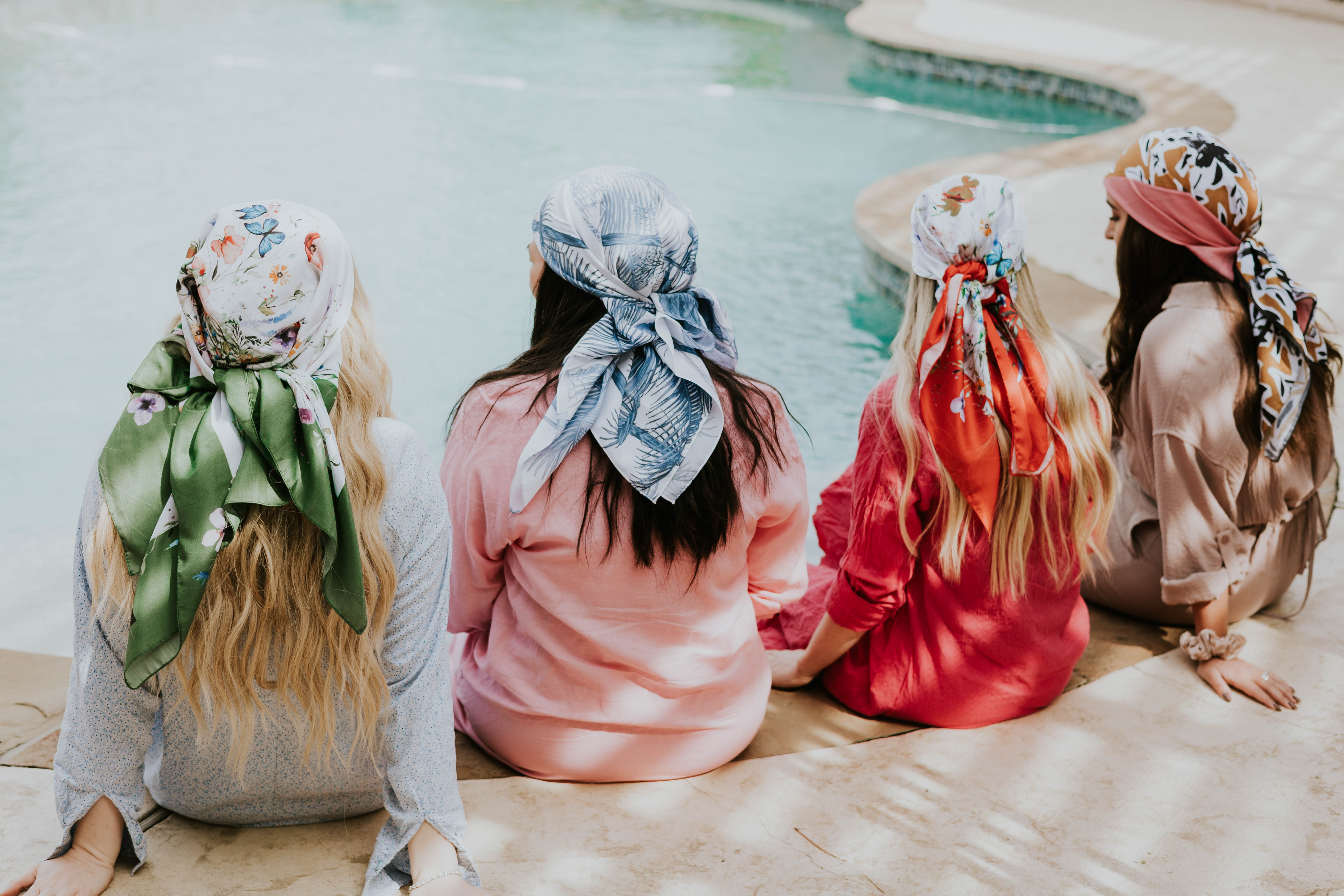 4 women sitting on the edge of a pool wearing fashionable head scarves 